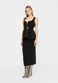 Must kohandatud kleit, millel on liibuv ülakeha, sügav dekoltee ja vöö; kombineeritud põlveni ulatuvate madu-nahaga mustriga saapadega.