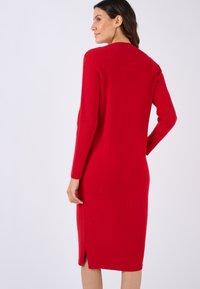 Abito a maglia rosso a coste con maniche lunghe, lunghezza a metà polpaccio e una fessura laterale. Tessuto testurizzato, design aderente, scollatura minimalista.