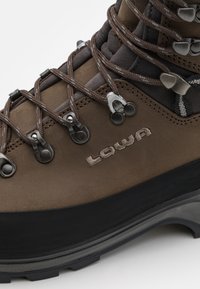 Bruine leren wandelschoen met metalen hardware, ingewikkeld gevlochten ontwerp en zwarte rubberen zool. Heeft geborduurde branding aan de zijkant.
