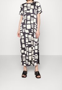 Vestido maxi de estampado en blanco y negro con mangas cortas, que presenta diseños de trazos de pincel rectangulares y aberturas laterales para facilitar el movimiento.
