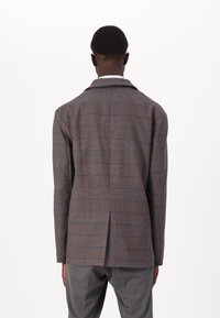 Brun rutete blazer med blå og oransje linjer, med en enkelt ventil og tradisjonelle revers. Stoffet ser teksturert og skreddersydd ut.