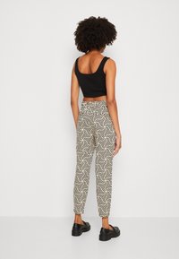 Zwarte cropped top gecombineerd met hoge, witte broeken met een geometrisch zwart patroon. Model draagt zwarte schoenen.