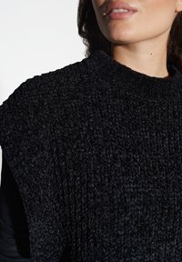 Indumento a maglia nera con texture, dotato di un collo alto e con un motivo a costine. Il materiale sembra morbido e accogliente, adatto per essere indossato a strati.