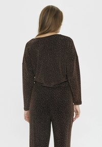 Abito marrone con trama e glitter metallici, caratterizzato da maniche lunghe e una vestibilità ampia. La parte posteriore ha un orlo curvo ed un design leggermente accorciato.