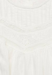 Witte katoenen top met textuur in verticale strepen, een kantafwerking met bloemenborduursel en geraffineerde stof bij de halslijn.