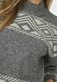 Pull en tricot gris avec un col montant, présenté avec un motif géométrique blanc. Texture douce et coupe décontractée.