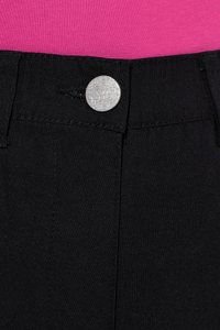 Nahaufnahme des schwarzen Hosenbunds mit silbernem Knopf mit der Aufschrift ‚PILAR POPE‘ und einem Teil des pinken Stoffs darüber.