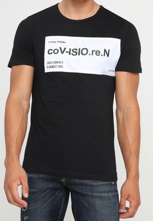 Homme portant un t-shirt noir avec une impression rectangulaire blanche affichant un texte déformé « coV-ISIO.re.N » et des chiffres sur la poitrine.