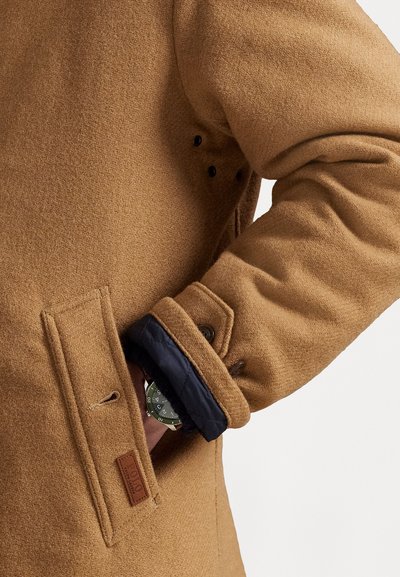 Bruine wollen mix jas met textuurstof, voorzien van een marineblauwe voering bij de mouwen en een leren logo patch op de voork pocket.