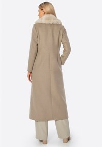 Lange beige jas met een bontkraag. Tailored ontwerp, rechte snit en lange mouwen. Gladde textuur, reikt tot halverwege de kuit.