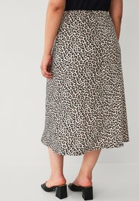 Leopardprint rok met een vloeiende ontwerp, voorzien van een beige achtergrond en donkere bruine vlekken, gecombineerd met zwarte block-heeled schoenen.