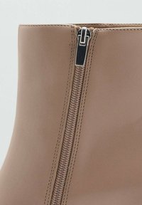 Bottine beige avec une texture lisse, dotée d'une fermeture éclair latérale en argent et de coutures contrastées le long de la couture.