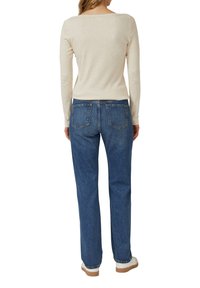 Beżowa bluzka z długim rękawem i dekoltem w kształcie łódki z tyłu, w połączeniu z niebieskimi jeansami o prostych nogawkach, z dwoma tylnymi kieszeniami i detalami szwów.