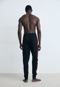 Zwarte sweatpants met een tapered fit, elastische tailleband en rode zijstrepen. Soepele textuur met zichtbare stikseldetails.