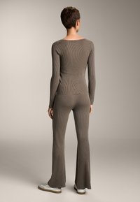 Barna bordázott kötött hosszú ujjú felső és trapéznadrág puha anyagból. Kiemelkedő részletek közé tartozik a testhez álló kialakítás és a sima, texturált szövet.