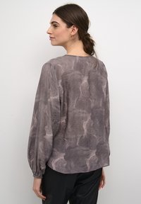 Srajca z dolgimi rokavi v svetlo sivi barvi z teksturiranim, abstraktnim vzorcem. Mehka tkanina z ohlapnim krojem in nabranimi rokavi.