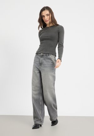 Grå ribbet langermet topp med rå kant, parret med vide grå jeans med subtil falming, iført svarte spisse hæler.