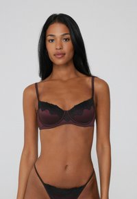Burgundy lace bra with black lace trim. Underwire design features adjustable straps and a smooth satin finish, highlighting intricate lace details.