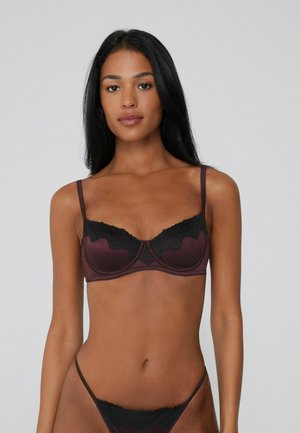 Reggiseno in pizzo bordeaux con bordi in pizzo nero. Il design con ferretto presenta spalline regolabili e una finitura in satin liscia, evidenziando dettagli intricati in pizzo.