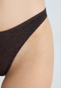 Bas de bikini en métal brun foncé avec une finition texturée, arborant une fine bande à la taille et des découpes hautes pour les jambes.