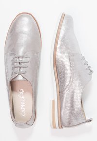 Chaussures à lacets en cuir argenté perforé avec un bout arrondi, une semelle intermédiaire blanche et une semelle accentuée de couleur marron clair. Présentent une texture lisse.