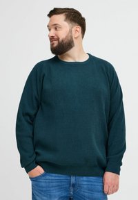 Tumes roheline kootud sviiter ümmarguse kaelusega, tekstureeritud pind ja lõdva istuvusega. Kantud siniste teksadega, ribidega mansettidega.