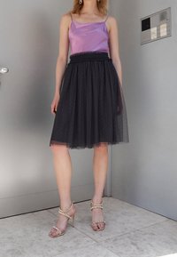Camisole di raso viola, gonna in tulle nero con pois e sandali con tacco alto decorati in oro. Dettagli di tessuti lisci e testurizzati visibili.