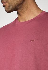 Ροζ βαμβακερό t-shirt με στρογγυλή λαιμόκοψη, με μικρό κόκκινο λογότυπο Nike στο αρισ τερό στήθος. Λείο ύφασμα, casual σχεδιασμός.