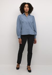 Lichtblauw overhemd met lange, gewatteerde mouwen. Gepaarde met zwarte, goed passende broek en zwarte schoenen met enkelbandjes.