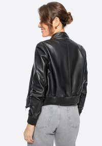 Černá kožená bomberka s žebrovanými manžetami a spodním lemem. Vyznačuje se hladkým povrchem a přiléhavým střih, zobrazená zezadu s šedými džínami.