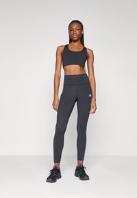 Deportiva negra y leggins de cintura alta hechos de material elástico, con un diseño ajustado y un sutil detalle del logo, combinados con zapatillas negras.