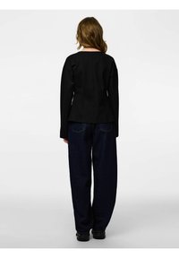 Juoda aptempianti striukė ilgomis rankovėmis, aukštu kaklu ir struktūruotu dizainu. Derinama su laisvomis tamsiomis džinsinėmis kelnėmis ir juodiems batams.