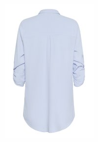 Chemise bleu clair à manches longues retroussées, pince au dos visible et ourlet incurvé.