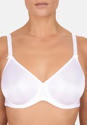 Vrouw draagt een witte, naadloze beugelbeha met verstelbare bandjes en kleine strikjes bij de bandjes tegen een effen achtergrond.