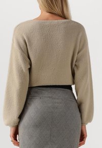 Beige, fuzzy, cropped trui met licht verlaagde schouders, gecombineerd met een hoog weergegeven, grijze rok met diamantenpatroon.