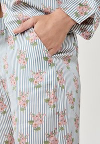 Pyjamastel in lichtblauw en witte strepen met bloemenpatroon, featuring roze bloemen en groene bladeren. Inclusief een zakdetail.