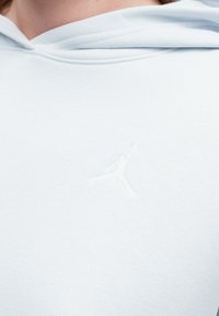 Jasnoniebieska bluza z kapturem, wykonana z miękkiego materiału, z białym haftowanym logo Jumpman na klatce piersiowej. Gładka struktura oraz luźny krój.