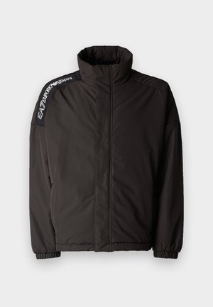 Zwarte gewatteerde jas met hoge kraag, elastische manchetten en logo-detail op de schouder. Beschikt over een gladde, matte afwerking en een relaxte pasvorm.