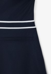 Prenda azul marino con tejido texturizado, dos franjas blancas a lo largo de la cintura y un detalle discreto de bolsillo lateral.