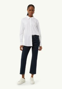 White button-up shirt with long sleeves, paired with dark blue cropped jeans and white sneakers. Simple design with no visible patterns.