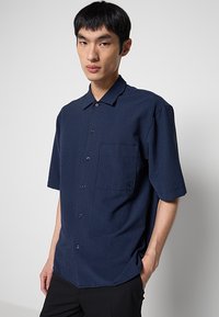 Camisa de manga corta con rayas azul marino, con cuello, un bolsillo en el pecho y cierre de botones. Tejido ligero con un patrón texturizado.