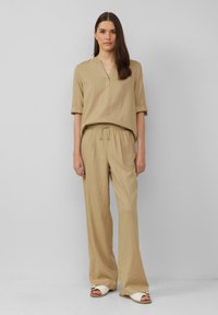 Beige linnen top met een V-hals en opgerolde mouwen, gecombineerd met bijpassende losse broek met elastische tailleband. Eenvoudige sandalen.