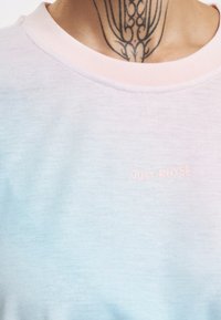 Světle modré tričko s krátkými rukávy, kulatým výstřihem a jemným vyšívaným logem "JUST RHYSE" v pastelově růžové barvě.
