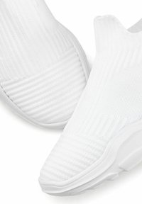 White slip-on shoes with a textured knitted upper, ribbed design along the sides, and white rubber sole featuring a subtle tread pattern.