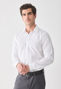 Witte langemouwen shirt met een spitskraag en knoopsluiting. Soepele textuur, gecombineerd met grijze op maat gemaakte broeken en een zwarte riem.