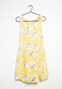 Gul ärmlös klänning med blommönster i grått och vitt, med knäppning fram, samlad midja och en utsvängd kjoldesign.