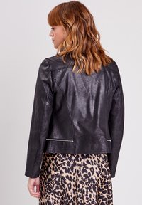 Veste en simili cuir noir au design ajusté, texture matelassée au dos et accents de fermeture éclair argentés, associée à une jupe imprimé léopard.