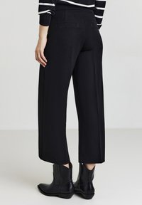 Pantaloni neri a gamba larga con una trama liscia, dotati di tasche laterali e vita alta, abbinati a eleganti stivaletti neri sopra alla caviglia.