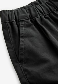 Gros plan sur un pantalon en tissu noir avec une taille élastique et une poche latérale, montrant les coutures détaillées et la texture.