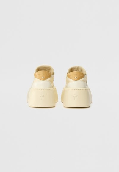 Platform sneakers in cream leather with a tan leather heel tab. Features a rounded toe, stitched details, and a branded signature on the side.